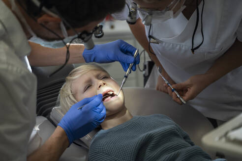 Zahnarzt untersucht die Zähne eines Patienten in der Nähe der Assistentin in der Klinik - NJAF00746