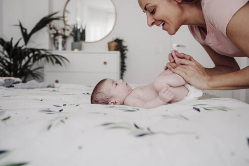 Happy mother playing with baby girl on bed at home - EBBF08342
