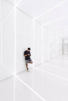 Junger Mann benutzt Smartphone in modernem Korridor - MMPF01219
