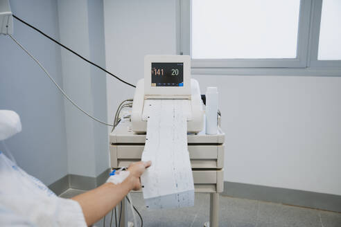 Hand of woman holding medical test report in delivery room - EBBF08344