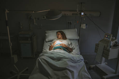 Pregnant woman sleeping on bed near equipment in hospital - EBBF08345