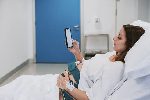 Pregnant woman using smart phone in hospital room - EBBF08350