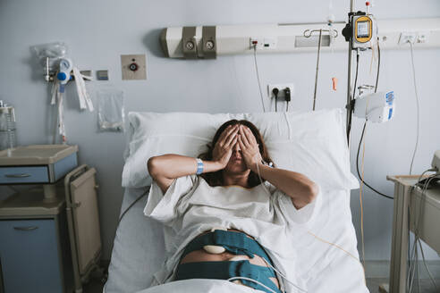 Stressed pregnant woman lying on bed in hospital - EBBF08352