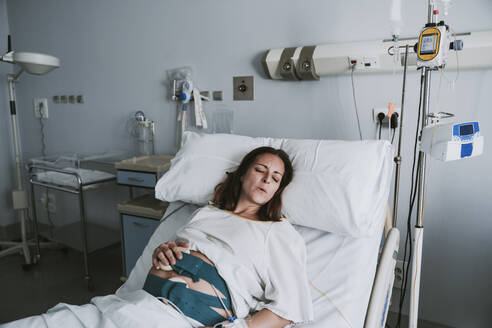 Schwangere Frau mit Schmerzen auf dem Krankenhausbett liegend - EBBF08353