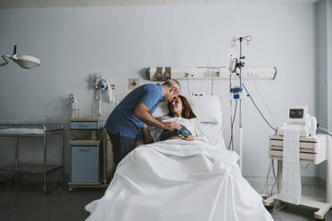 Mann umarmt schwangere Frau auf dem Bett im Krankenhaus - EBBF08356