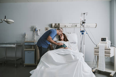 Man embracing pregnant woman on bed in hospital - EBBF08356