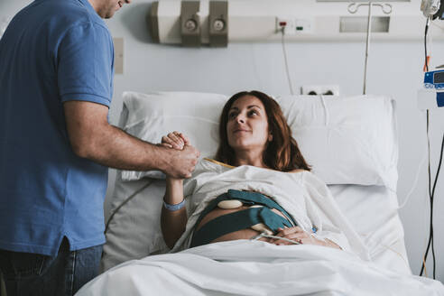 Man consoling pregnant woman on bed at hospital - EBBF08357