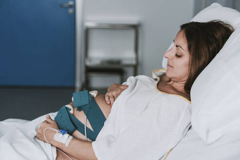 Pregnant woman with hands on stomach lying in hospital - EBBF08363