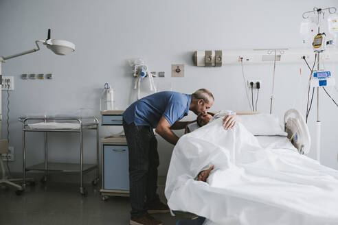 Man kissing woman lying on bed in hospital - EBBF08365