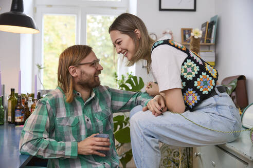 Happy man holding coffee cup and sitting with woman at home - SUF00717