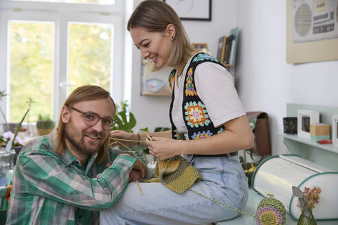 Smiling woman knitting near man sitting at home - SUF00719