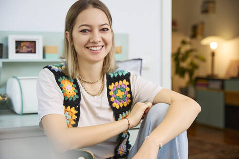 Happy woman wearing knitted jacket and sitting at home - SUF00725