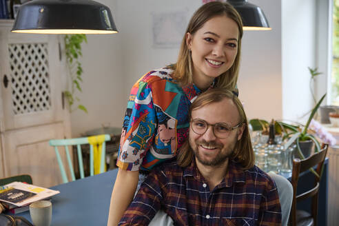 Smiling man with young woman sitting on dining table at home - SUF00734