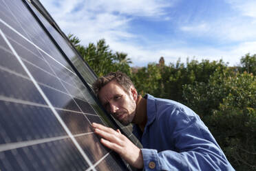 Man examining and touching solar panels under cloudy sky - JOSEF23108