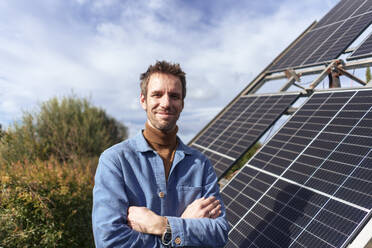 Smiling mature man standing near solar panels on sunny day - JOSEF23114