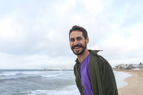 Happy man standing at beach under cloudy sky - JOSEF23121
