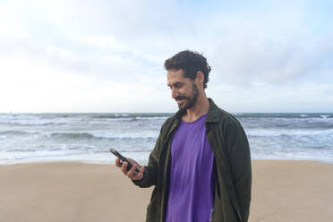 Lächelnder Mann mit Mobiltelefon am Strand - JOSEF23133