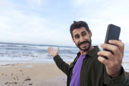 Glücklicher Mann zeigt Strand auf Videoanruf durch Smartphone - JOSEF23143