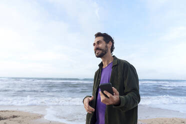 Lächelnder Mann mit Mobiltelefon am Strand - JOSEF23146