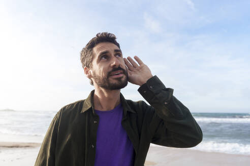 Man listening under sky at beach on sunny day - JOSEF23152