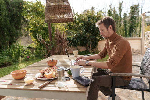 Freelancer working on laptop near food at table - JOSEF23165