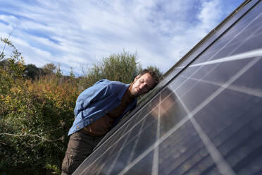 Man leaning on solar panel with eyes closed on sunny day - JOSEF23166