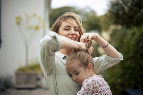 Lächelnde Frau bindet die Haare ihrer Tochter mit einem Haargummi zusammen - JOSEF23169