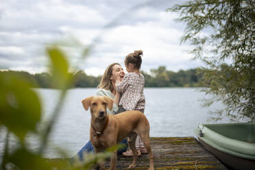 Glückliche Frau hat Spaß mit Tochter in der Nähe von Hund vor See - JOSEF23174