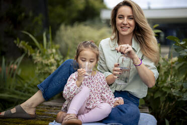 Smiling mother with daughter drinking water on pier - JOSEF23196