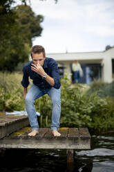 Man holding breath and preparing to jump in lake water on jetty - JOSEF23198