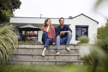 Smiling woman looking at man in front of house - JOSEF23255