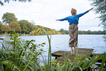 Glückliche Frau mit ausgestreckten Armen, die auf einen Pier springt - JOSEF23282