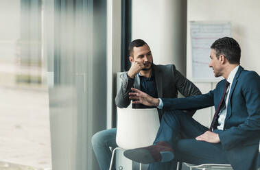 Businessman talking with colleague sitting in office - UUF31115