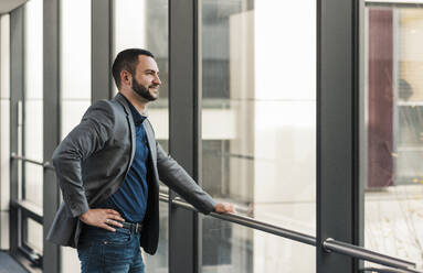 Smiling businessman looking out of window in office - UUF31119