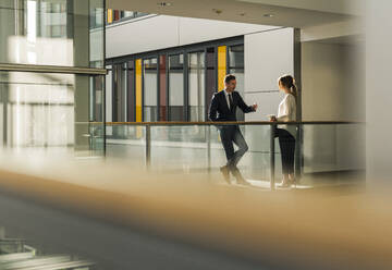 Businessman talking to colleague on walkway at office - UUF31123