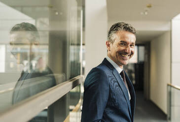 Smiling businessman near glass wall in office - UUF31126