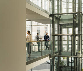 Coworkers talking on elevated walkway at office - UUF31128