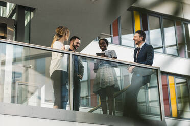 Happy coworkers talking on elevated walkway at office - UUF31129