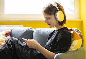 Girl listening to music through wireless headphones at home - NJAF00752