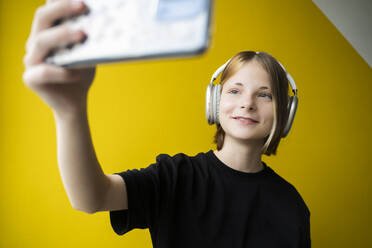 Smiling girl taking selfie in front of wall at home - NJAF00758