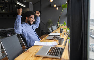 Successful businessman sitting with laptops at desk - VRAF00296