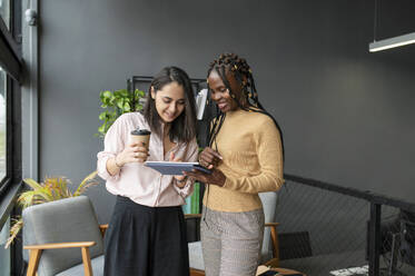 Geschäftsfrau hält eine Kaffeetasse und diskutiert mit einem Kollegen über einen Tablet-PC - VRAF00301