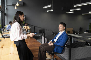 Businesswoman talking with colleague sitting in chair - VRAF00306