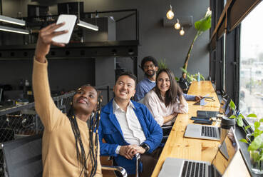 Smiling businesswoman taking selfie through smart phone with colleagues in office - VRAF00315