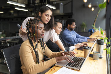 Geschäftsfrauen und Geschäftsmänner arbeiten an Laptops am Schreibtisch - VRAF00318