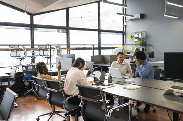 Business people discussing and working on laptop at desk - VRAF00366