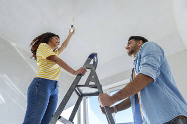 Smiling man helping woman in installing light bulb at home - AAZF01446