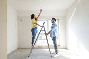 Junges Paar benutzt eine Leiter und installiert eine Glühbirne in einem neuen Haus - AAZF01447