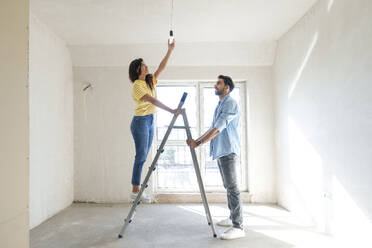 Young couple using ladder and installing light bulb at new home - AAZF01447