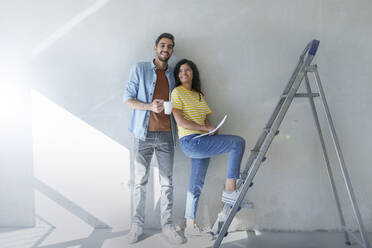 Ein glückliches Paar steht vor einer Mauer in der Nähe einer Leiter im neuen Haus - AAZF01455